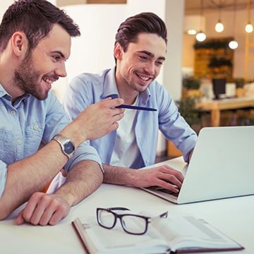 Two men looking at a computer at work, learning about their team's strengths.